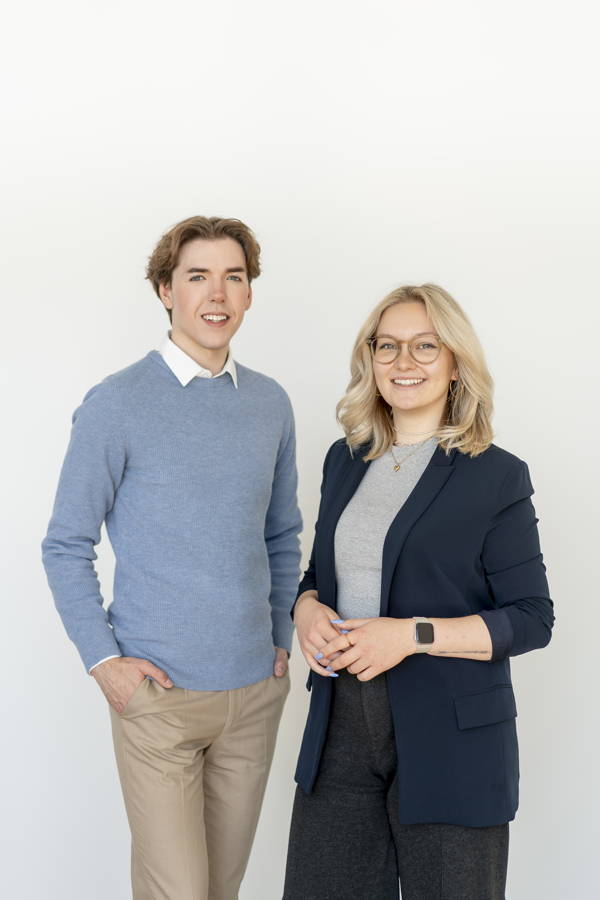 Zwei lächelnde Personen stehen vor weißem Hintergrund