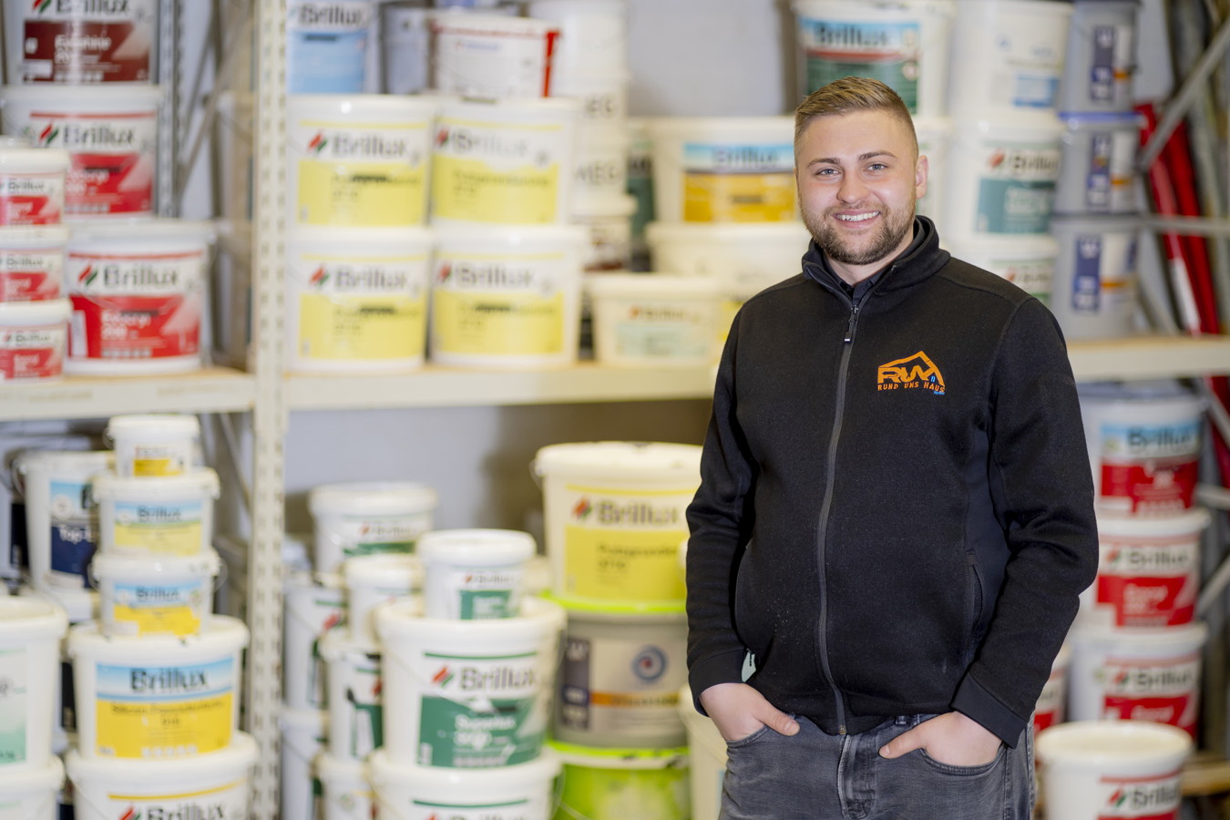 Mann steht vor Regalen mit Farbdosen in einem Baumarkt