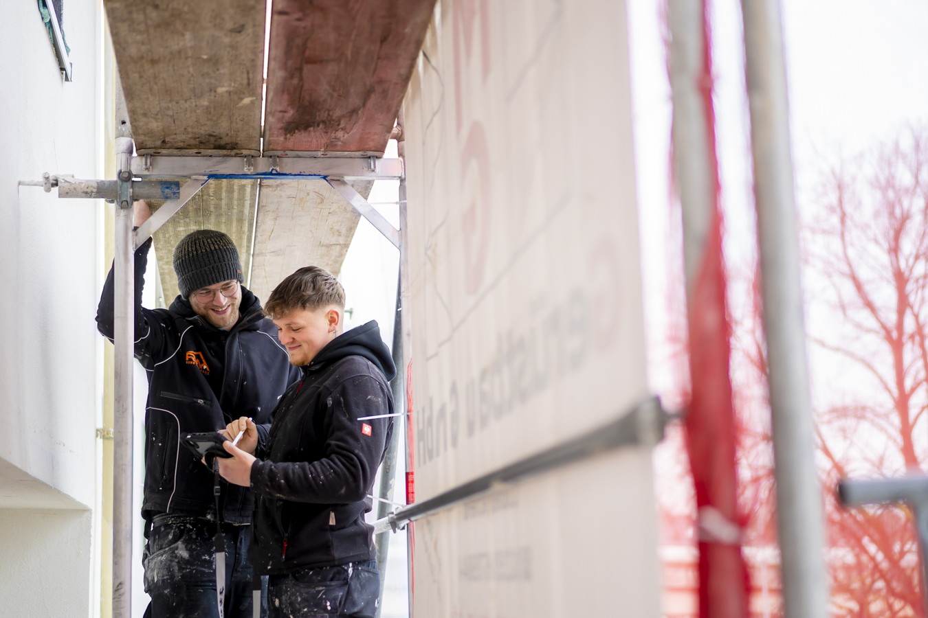 Zwei Handwerker auf einem Gerüst prüfen gemeinsam ein Tablet