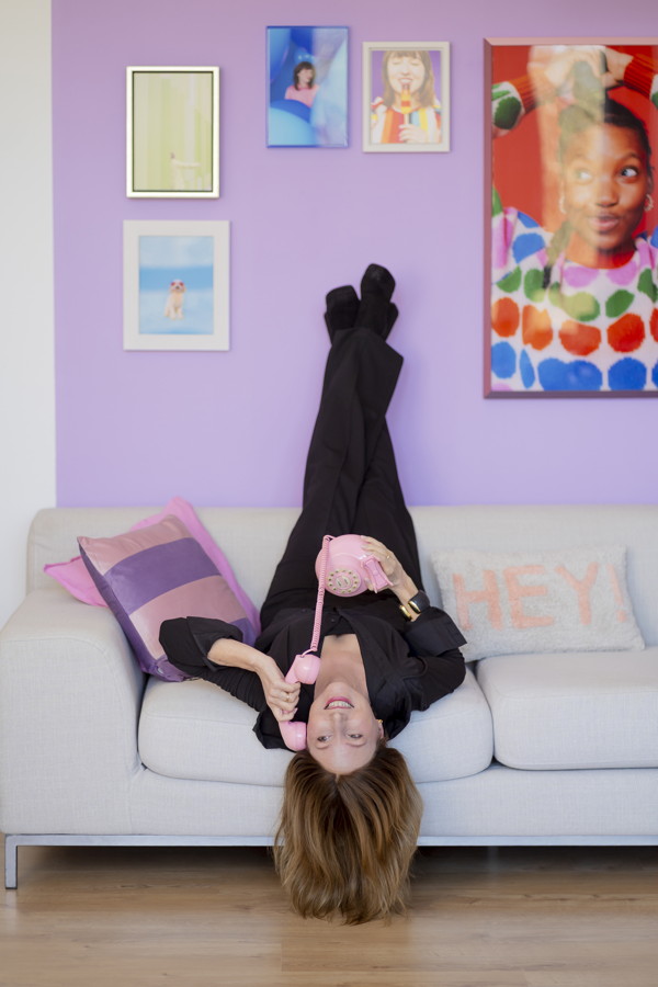 Frau liegt kopfüber auf einem Sofa und telefoniert mit einem rosa Telefon