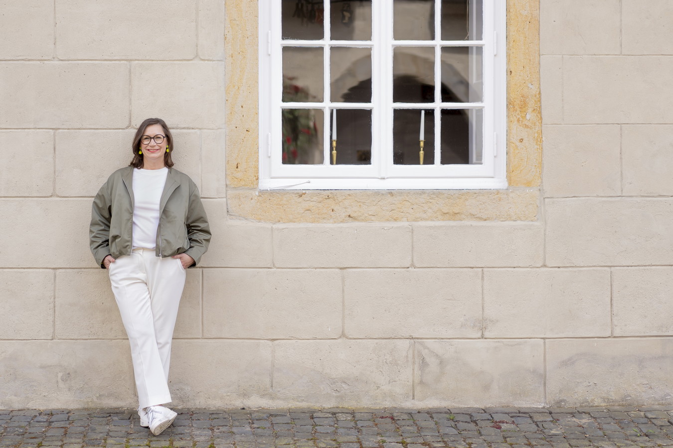 Frau lehnt an einer hellen Steinwand unter einem Fenster