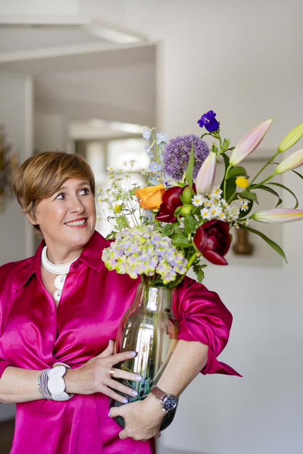 Frau in pinker Bluse hält einen großen Blumenstrauß in einer Vase