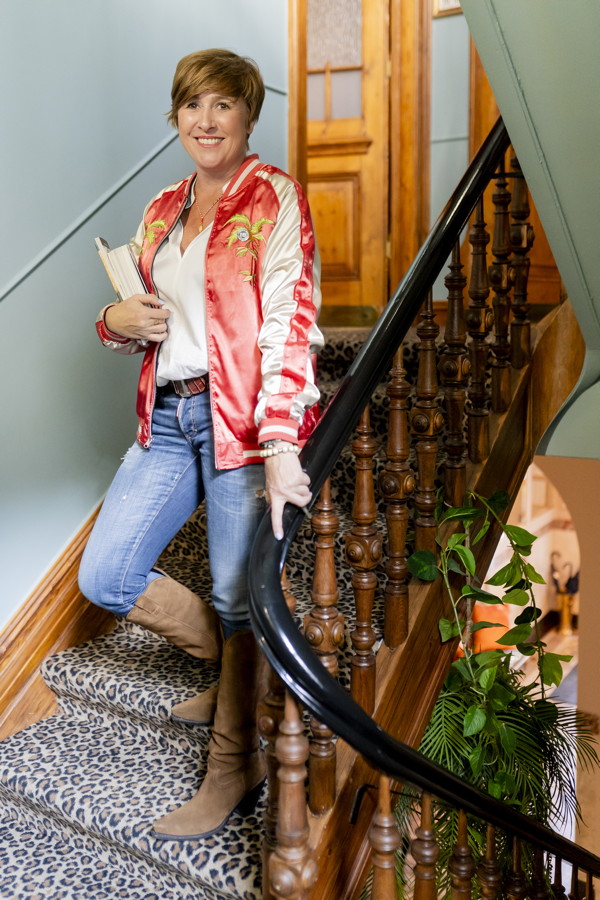 Frau auf einer Treppe mit Leopardenmuster-Teppich, hält Bücher und lächelt in die Kamera