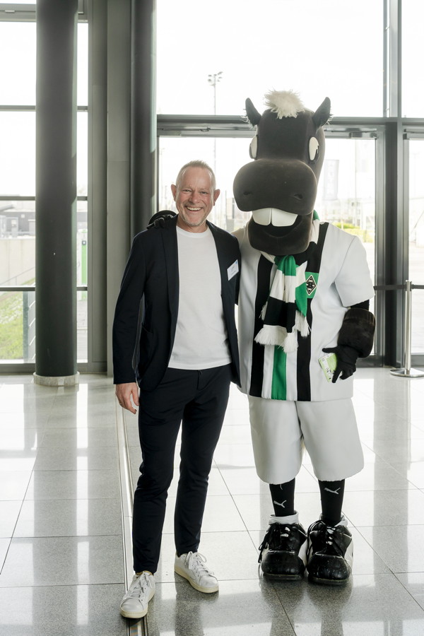 Ein Mann steht neben dem Borussia-Mönchengladbach-Maskottchen Jünter in Vereinskleidung