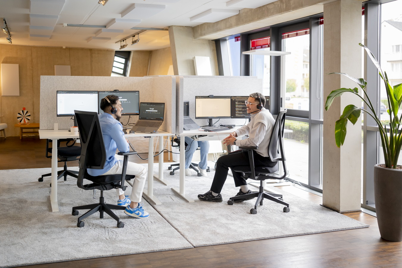 Zwei Mitarbeiter mit Headsets arbeiten an Schreibtischen in einem modernen Großraumbüro
