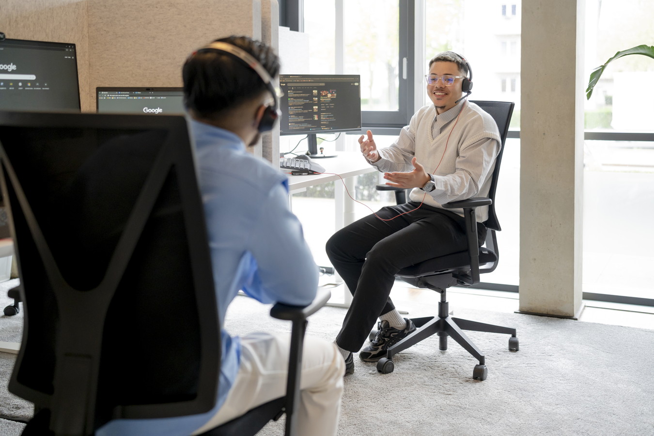 Zwei Kollegen mit Headsets sprechen in einem Büro an ihren Computern