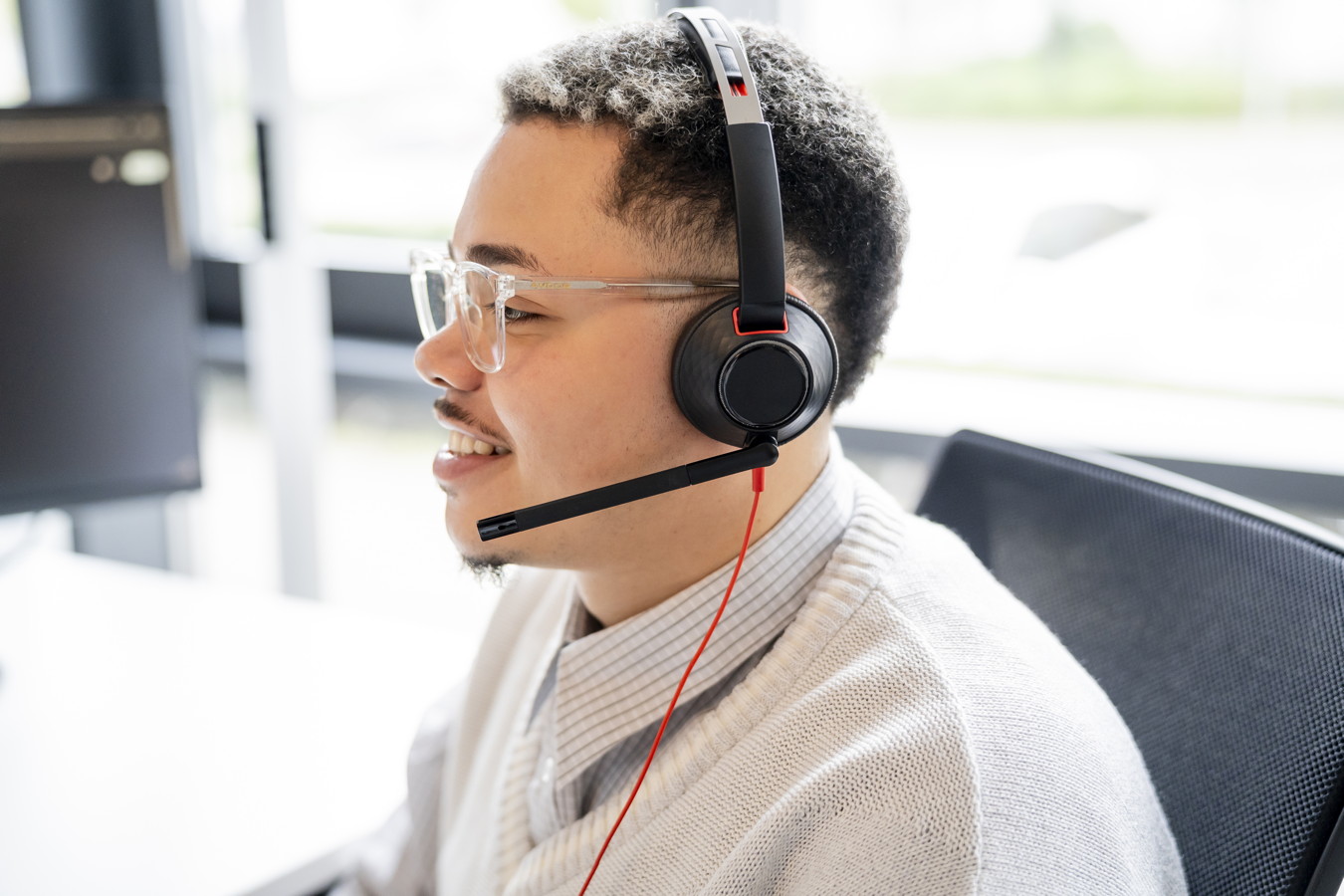 Mann mit Headset und Brille im Büro, lächelnd am Computer