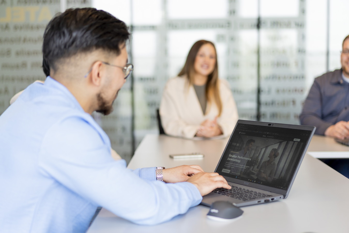 Mann arbeitet am Laptop in einer Besprechung mit zwei Kolleginnen und Kollegen