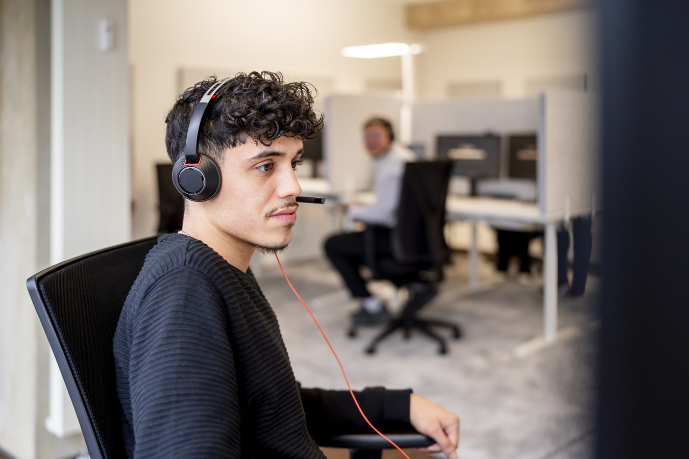 Businessfotos Mann mit Headset sitzt im Büro am Schreibtisch und arbeitet am Computer