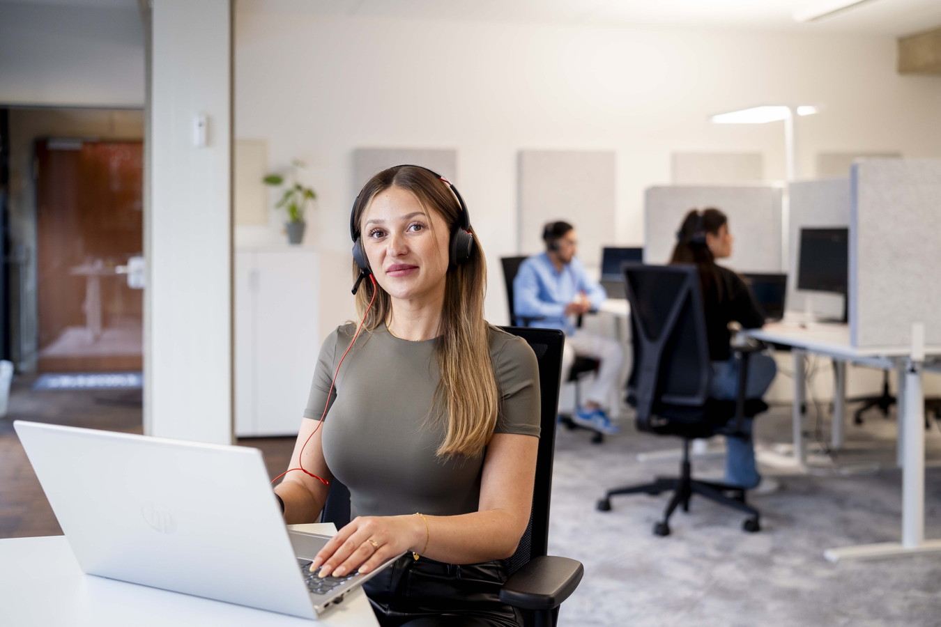 Frau mit Headset arbeitet am Laptop in einem Großraumbüro