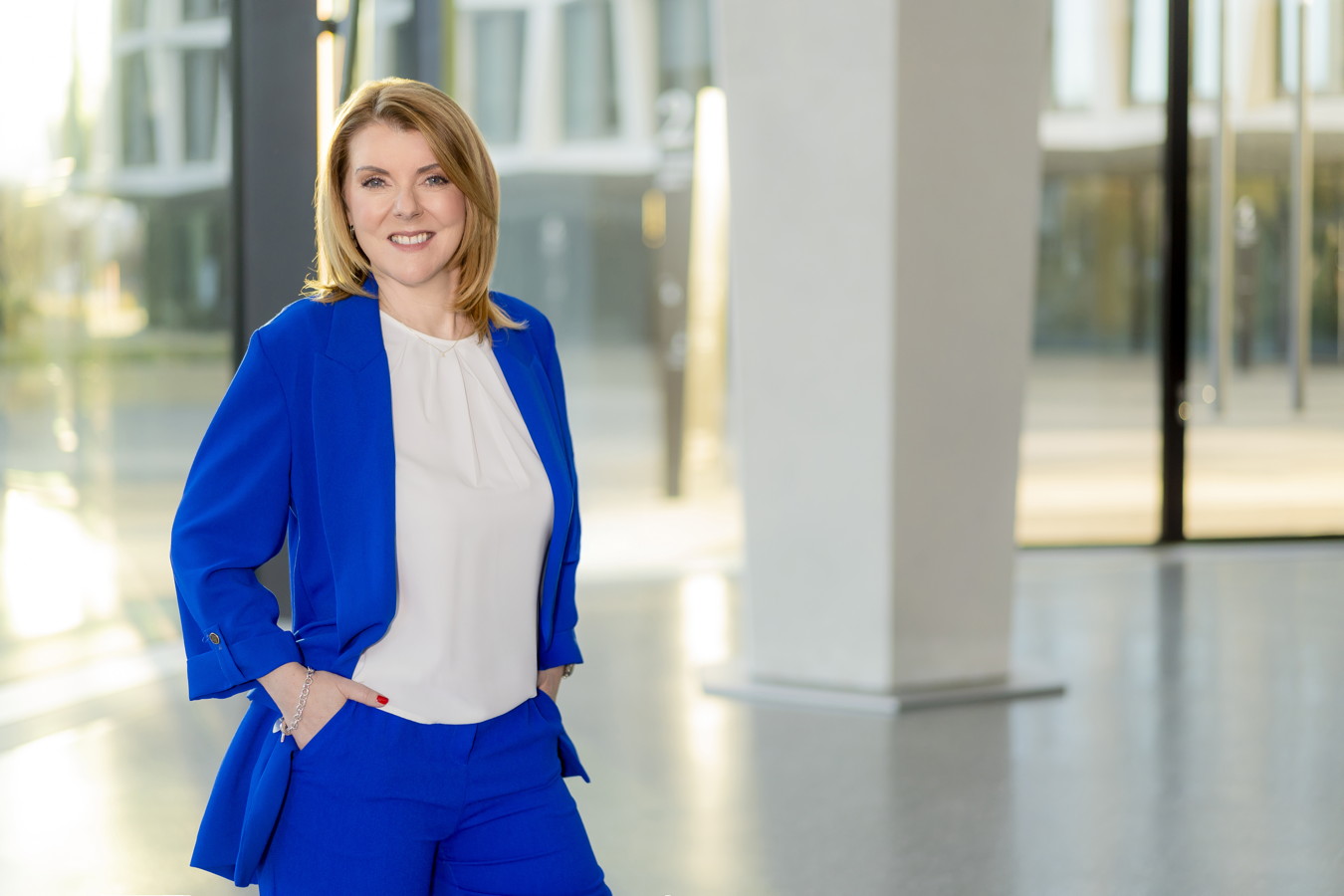 Porträt einer lächelnden Frau im blauen Anzug in einem hellen Innenraum