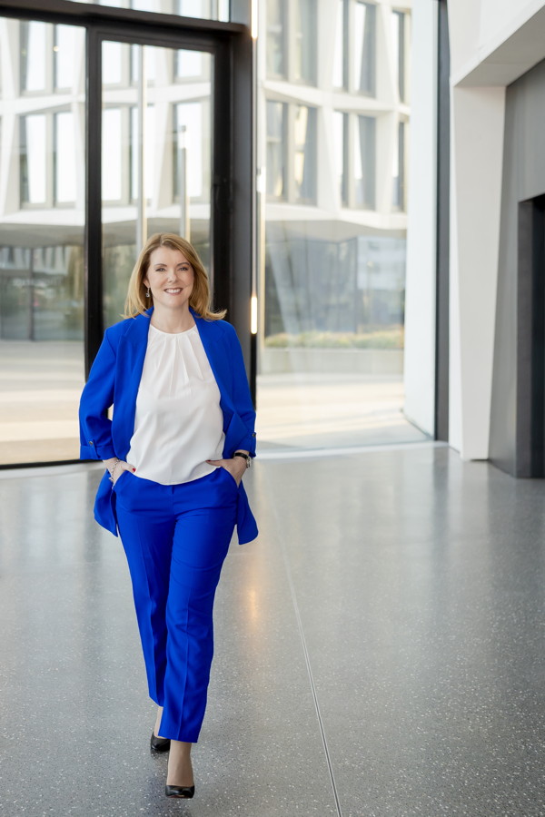 Frau im blauen Hosenanzug steht in einem modernen Gebäude