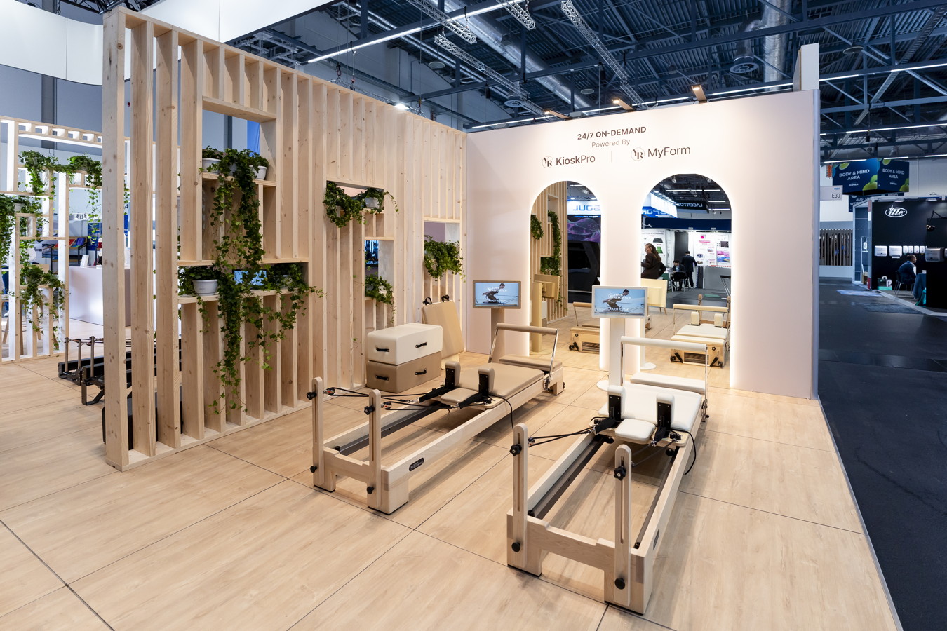 Messestand mit Holzverkleidung, Pflanzen und zwei Pilates-Geräten auf einer Messe