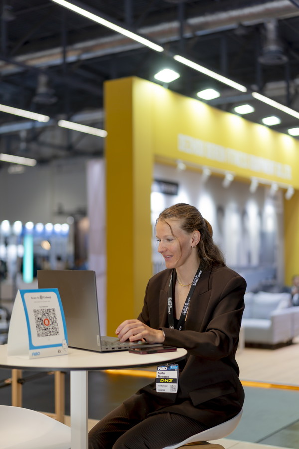 Frau arbeitet an einem Laptop an einem Messestand mit QR-Code-Schild