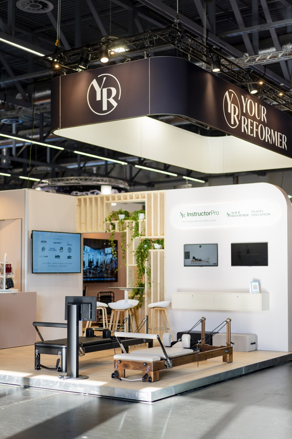 Messestand von Your Reformer mit Pilates-Geräten und Bildschirmen