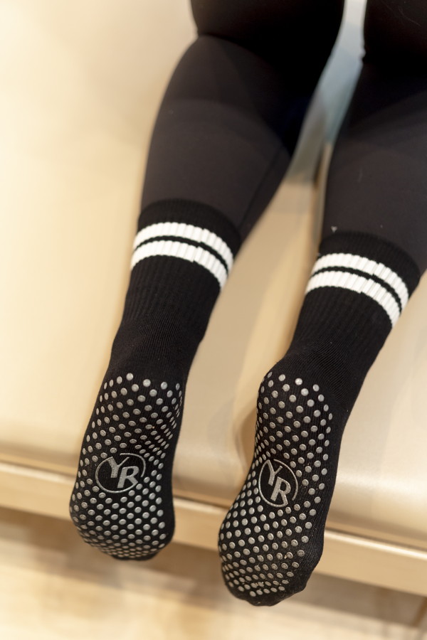 Beine mit schwarzen Socken und rutschfesten Sohlen, die von einer Bank hängen