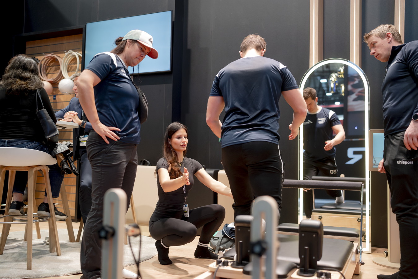 Mehrere Personen in einem Fitnessstudio oder Showroom bei einer Übungseinweisung an einem Trainingsgerät